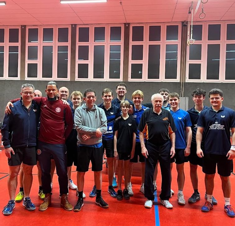 Gruppe junger Tischtennisspieler in blauen Т-Shirts vor einem Vereinshaus.