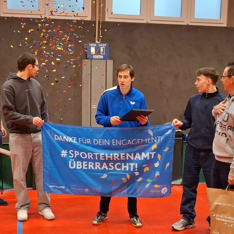 Zwei Männer stehen lächelnd nebeneinander vor einer grauen Wand.
