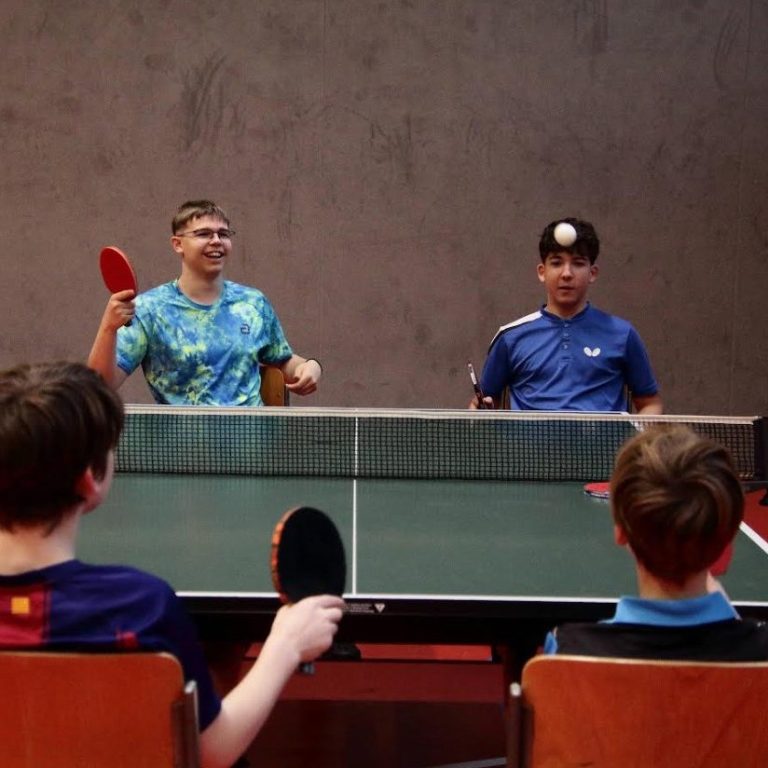 Gruppe junger Tischtennisspieler in blauen Т-Shirts vor einem Vereinshaus.