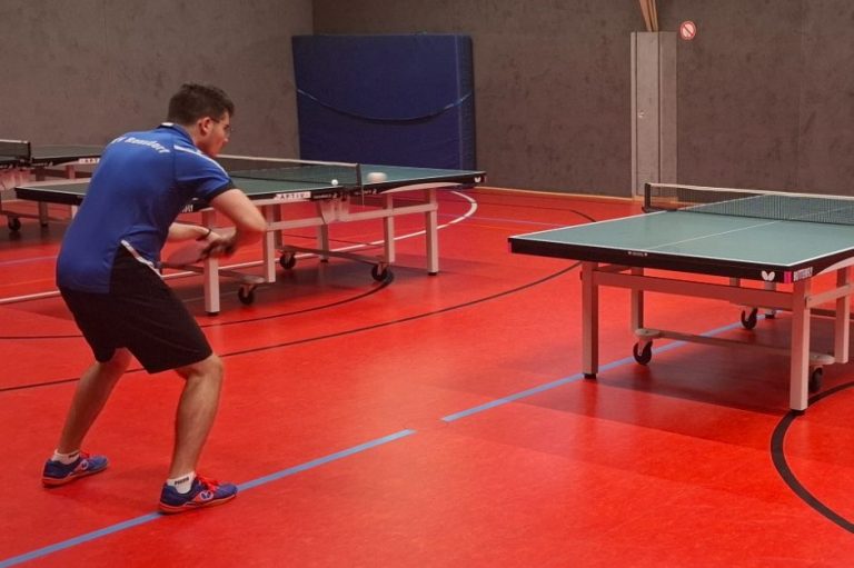 Ein Tischtennisspieler bereitet sich auf einen Schlag an einem Tisch mit rotem Boden vor.