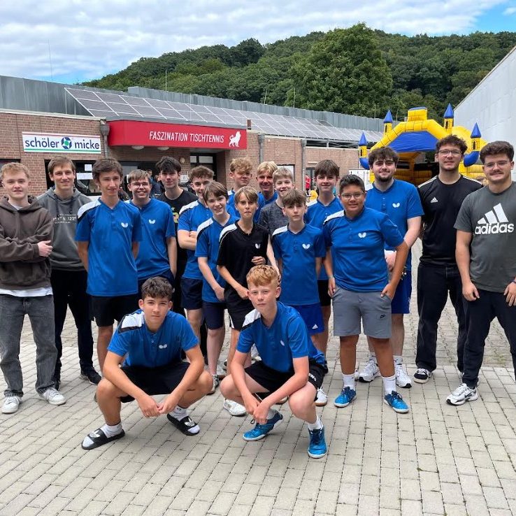 Gruppe junger Tischtennisspieler in blauen Т-Shirts vor einem Vereinshaus.